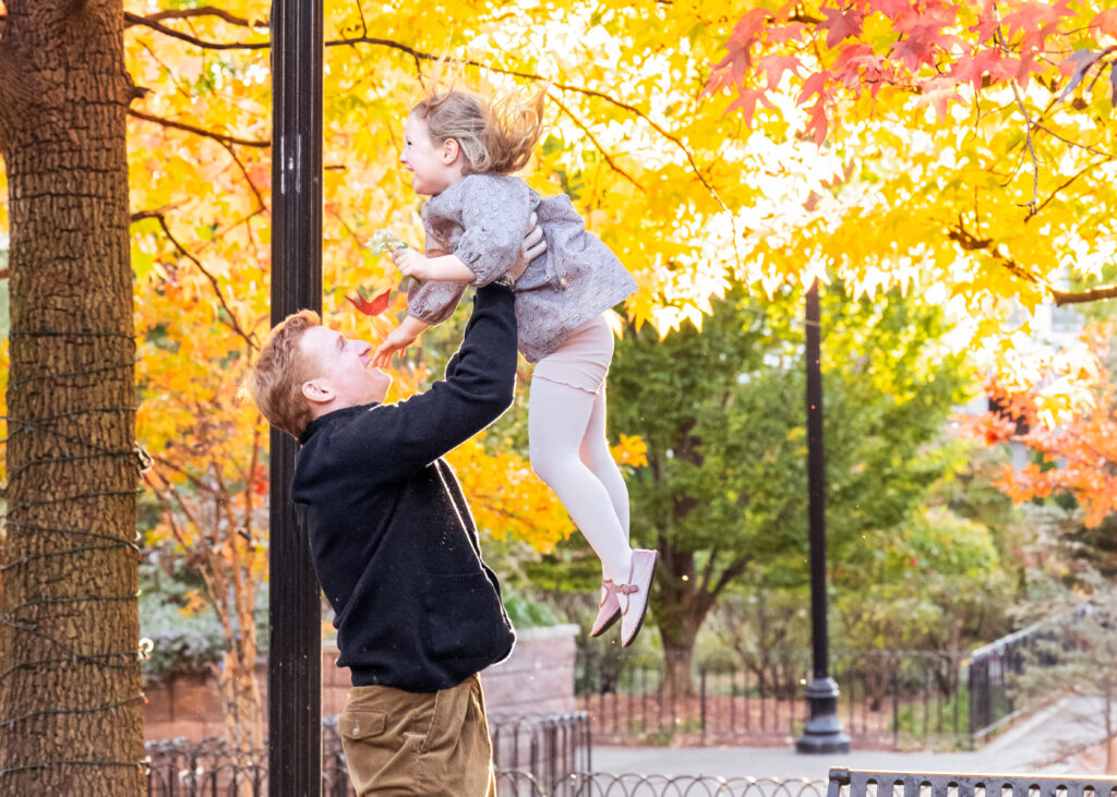Dad throwing girl into the air surrounded by fall foliage during a family photo session 
