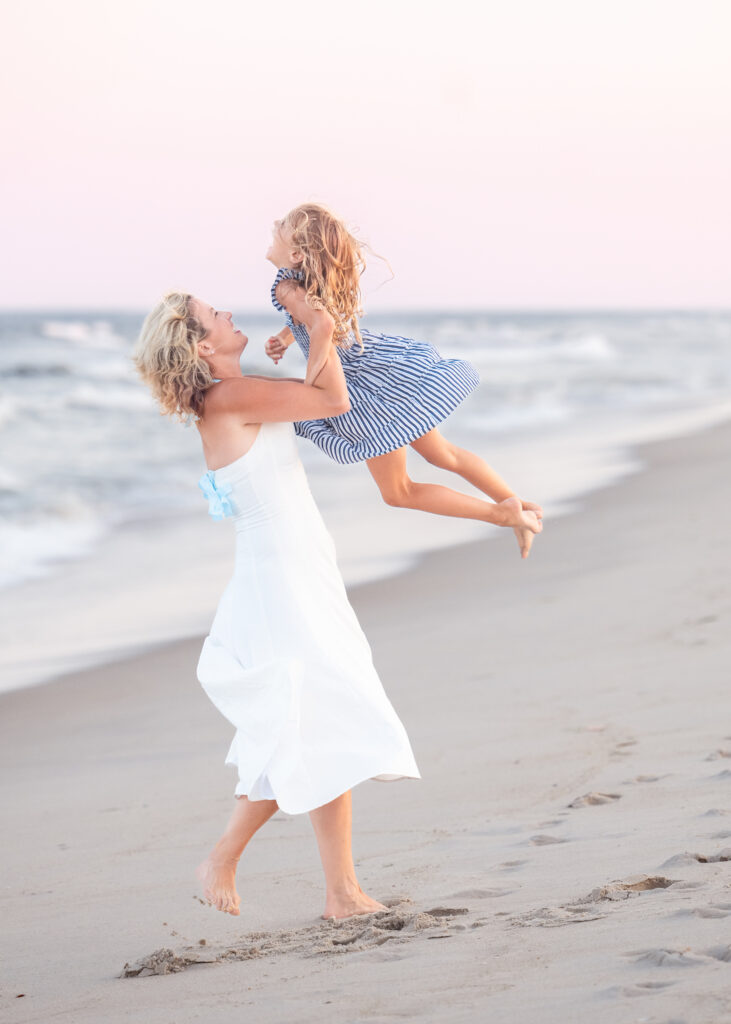Mother lifting her daughter in the air during a family photography session at the Jersey Shore.