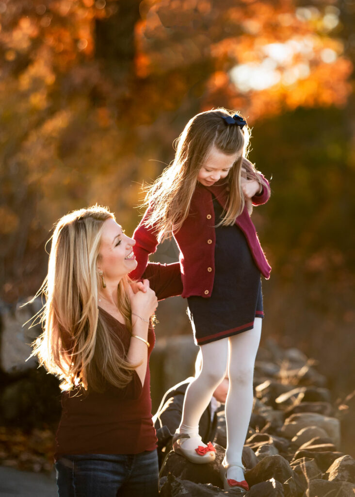 Mother helping her daughter balance on rocks during a family photography session at sunset in Hoboken, New Jersey.